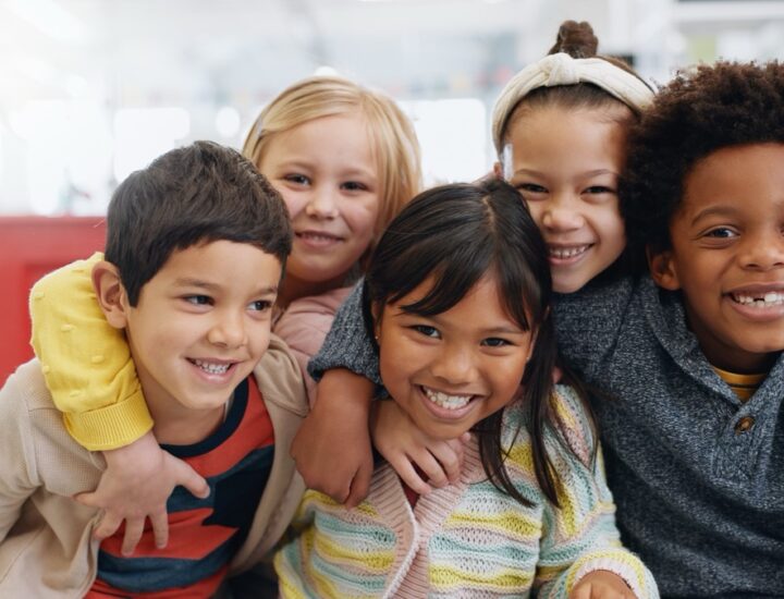 A group of elementary school students crowds together with their arms around one another.
