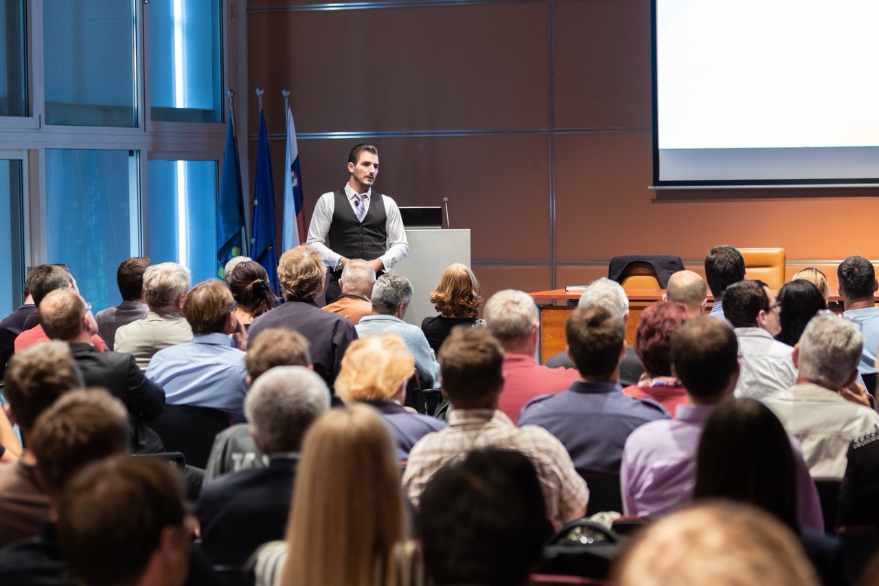 A man speaks in front of an audience at a seminar. 