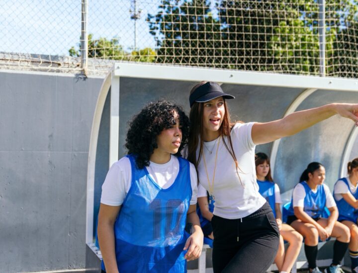 Coach gives instructions to a youth soccer player while teammates wait on the bench.